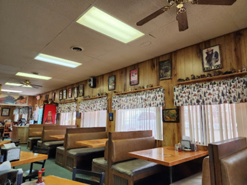 Interior of a cozy diner with wooden walls, booths, and decorative posters, featuring large windows with patterned curtains.